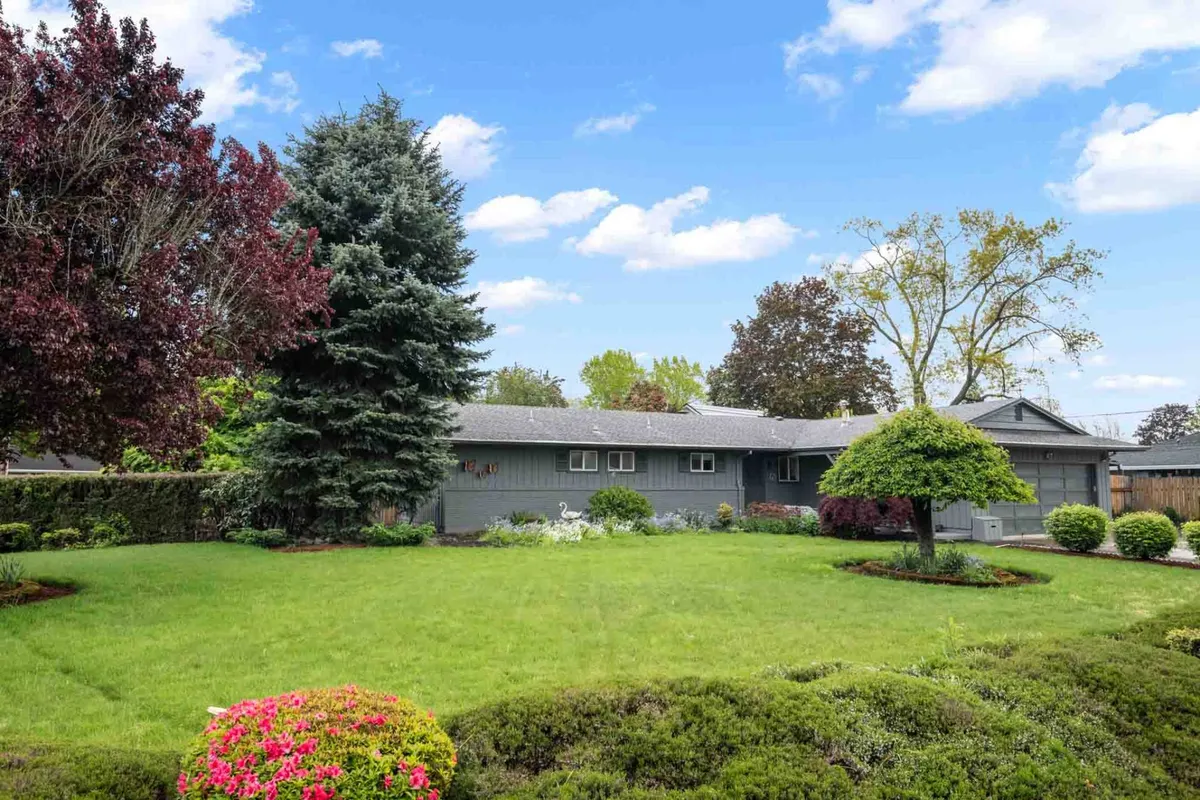 This exterior shot presents a manicured lawn, vibrant flower beds, and tall trees framing the house facade. The space is clearly designed for both relaxation and family gatherings, with ample lawn area for children to play and families to enjoy the outdoors together.