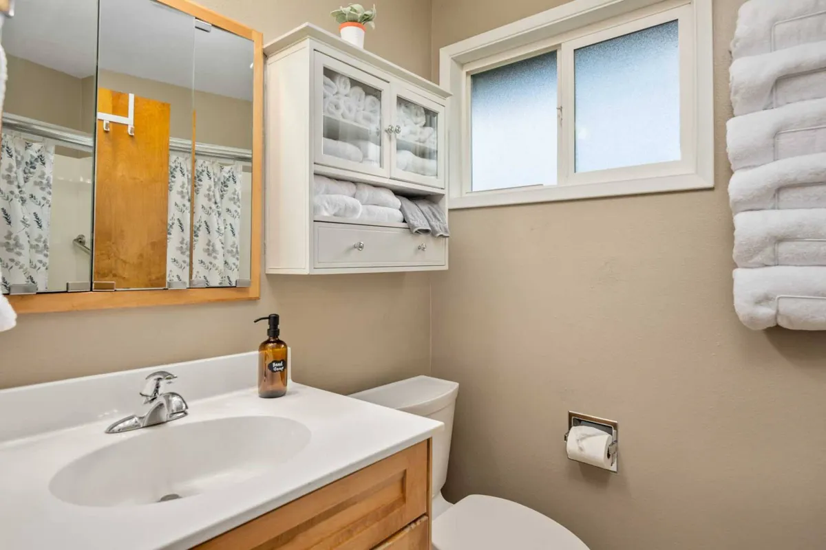 A modern bathroom featuring a large mirror, sink, ample towel storage, and a window that brings in soft daylight. The organized and uncluttered layout provides a spa-like atmosphere, ideal for personal care routines.