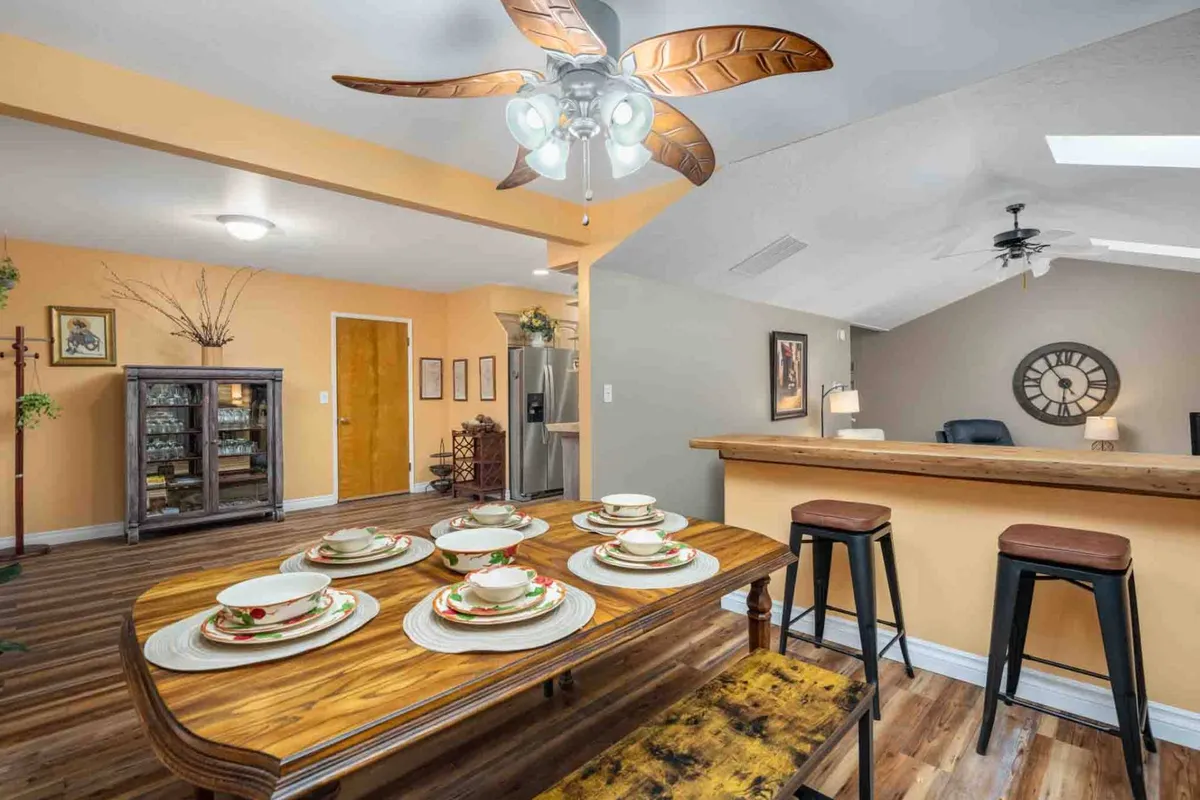 The image captures a cozy dining area featuring a large dining table set with plates, a visible bar area, a glass-front cabinet, and a ceiling fan overhead. The setting is ideal for family meals, entertaining guests, and hosting special dinners or brunches.