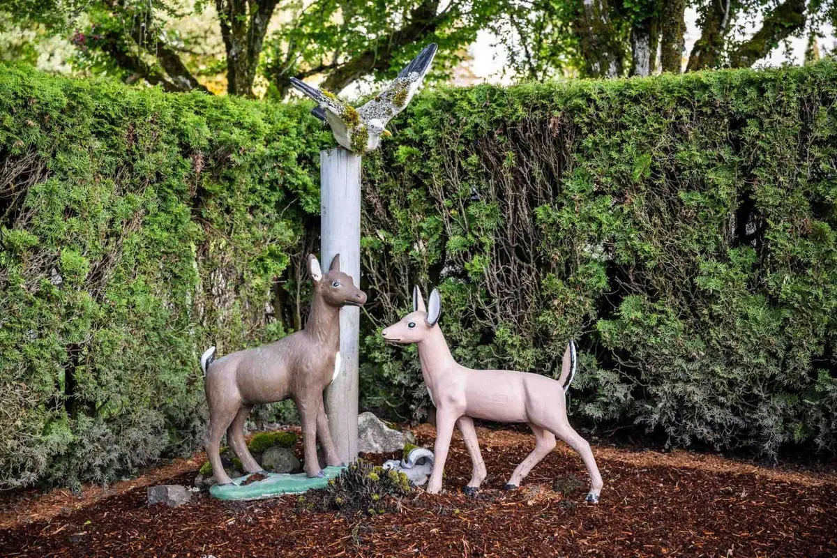 A whimsical outdoor garden scene with playful deer and bird sculptures nestled among lush green hedges, creating a lighthearted and nature-immersed atmosphere.