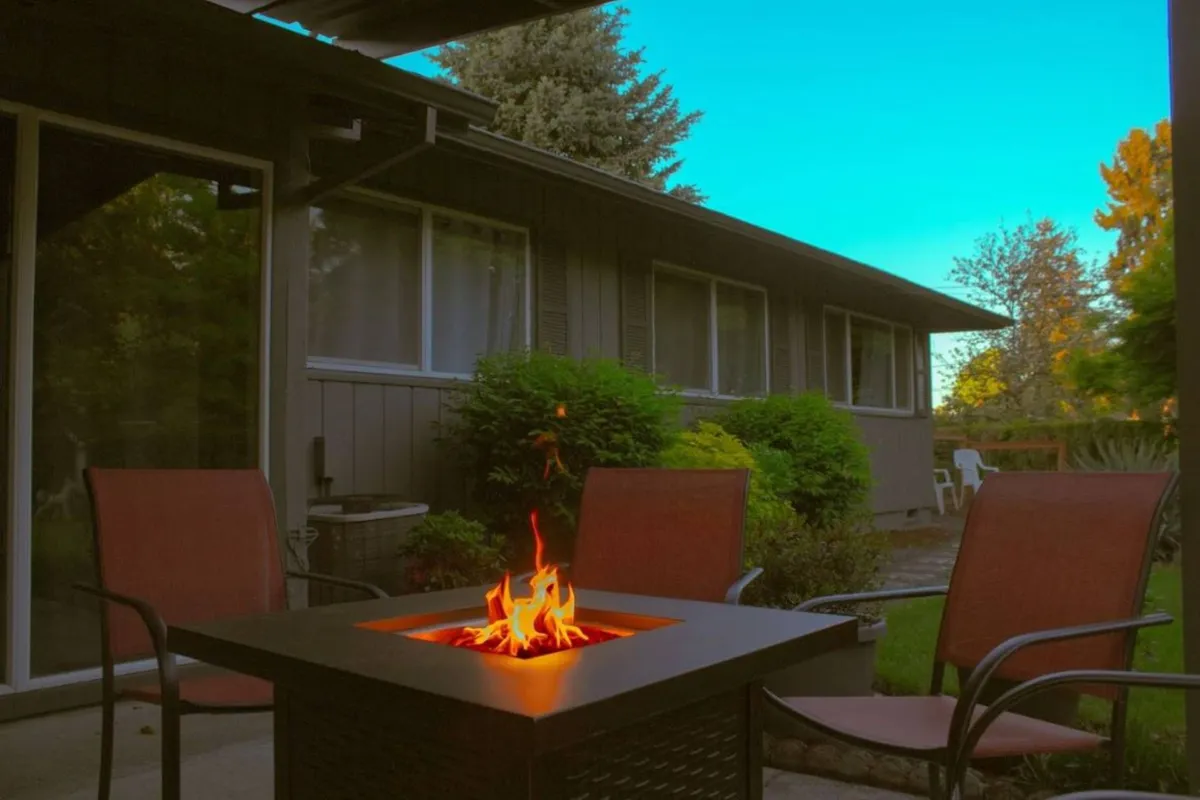 A beautifully landscaped backyard featuring a central fire pit surrounded by comfortable outdoor chairs, set amid lush greenery. The setting is perfect for evening gatherings, with a cozy, inviting atmosphere ideal for sharing stories, enjoying a glass of wine, or simply unwinding under the stars.