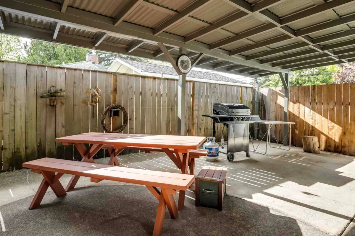 This image features a vibrant orange picnic table and a grill, set against a backdrop of secure fencing. The sunny yard invites guests to dine al fresco or relax outdoors, with the fence clearly visible to highlight the private and safe environment. The setup is perfect for gatherings, barbecues, and enjoying meals outside.